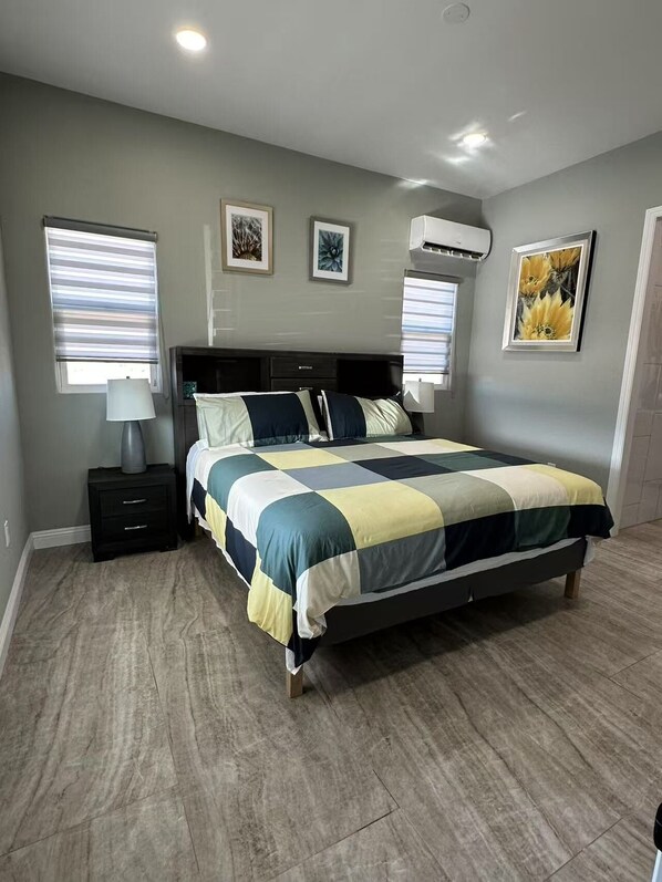 A bedroom with a bed, nightstands, a lamp, and wall-mounted air conditioning unit.