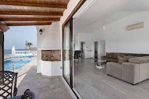 Un salon moderne avec un grand canapé, une porte en verre donnant sur une piscine et une vue sur un bâtiment blanc.