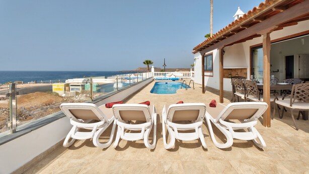Una terraza con sillones blancos, una piscina y vistas al mar.