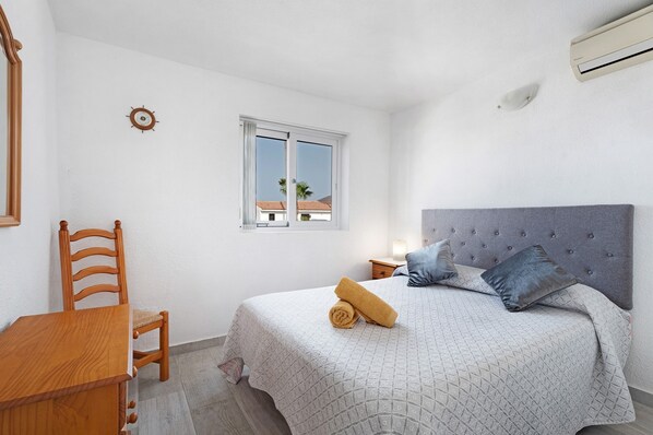 Un dormitorio con una cama, una silla, una mesa, un ventanal y un reloj de pared.