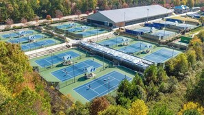 An outdoor tennis court complex with multiple courts, a large building, and surrounding trees. - Groovy Cary Crib - Pickleball, Pets & Plug-In 4 EV (Cary)