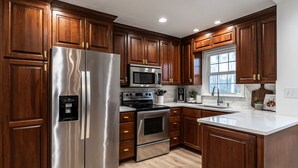 A modern kitchen with wooden cabinets, stainless steel appliances, and a marble countertop. - Groovy Cary Crib - Pickleball, Pets & Plug-In 4 EV (Cary)