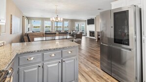 Una cocina amplia con encimera de granito, refrigerador de acero inoxidable y comedor con vista al exterior.