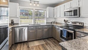 Una cocina moderna con electrodomésticos de acero inoxidable, armarios blancos y un amplio ventanal que proporciona luz natural.