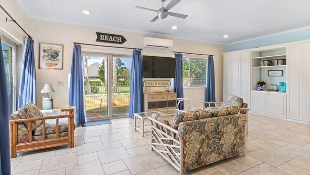 Un amplio salón con ventilador de techo, un sofá, una mesita y un letrero que dice "BEACH HOUSE".