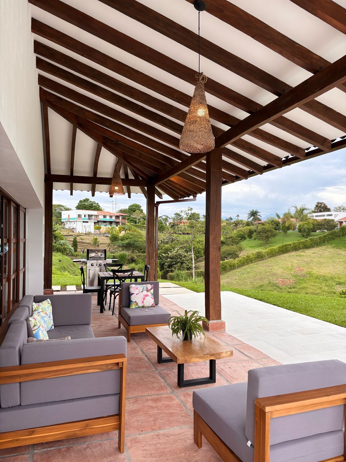 An outdoor patio with wooden furniture, a grill, and a view of a lush landscape.