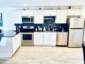 Una cocina moderna con armarios blancos, electrodomésticos de acero inoxidable, salpicadero de azulejos y piso de madera.