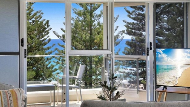 Ein Zimmer mit einer großen Schiebeglastür, die auf einen Balkon mit Blick auf Kiefern und Strand führt.