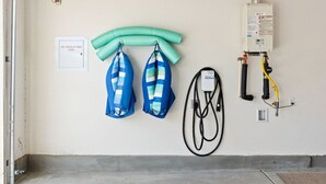 Une pièce équipée d’une colonne montante pour les extincteurs automatiques, de deux sacs à rayures bleues et blanches accrochés au mur, et d’un chauffe-eau avec des tuyaux.