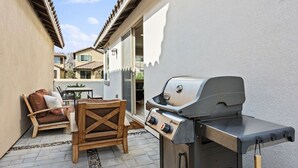Une terrasse avec un barbecue, du mobilier d’extérieur et une vue sur les bâtiments voisins.