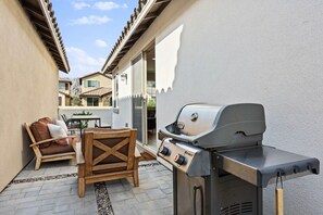Een terras met een barbecue, tuinmeubilair en uitzicht op omliggende gebouwen.