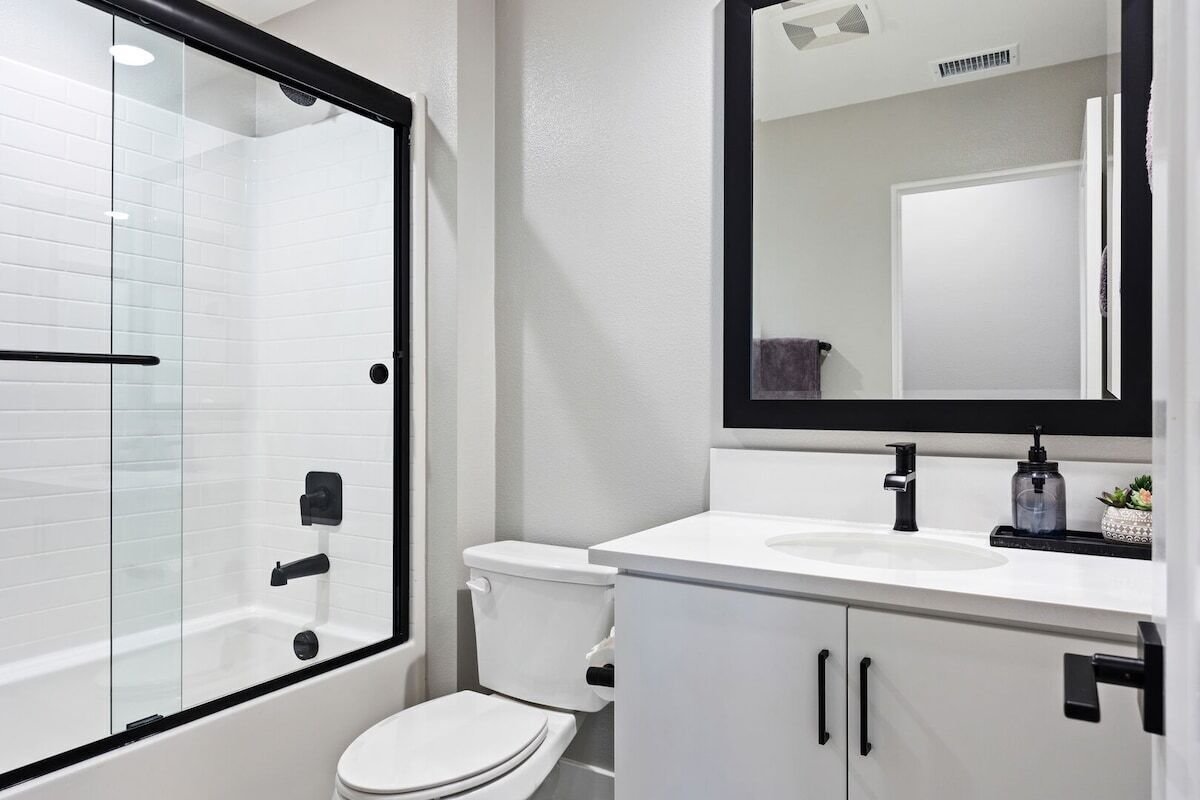 A modern bathroom with a glass-enclosed shower, a white toilet, and a white sink with a black faucet.