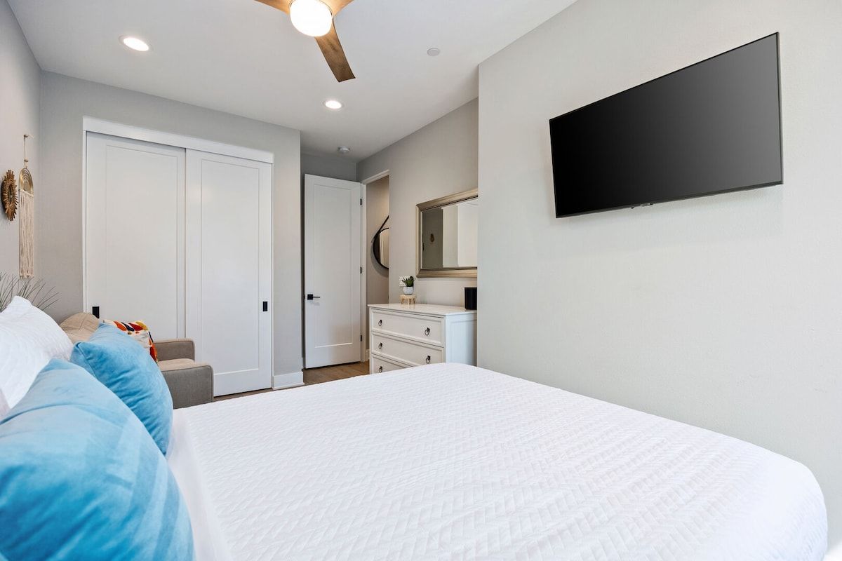 Une chambre à coucher comprenant un lit, une commode, un téléviseur fixé au mur et un ventilateur de plafond.