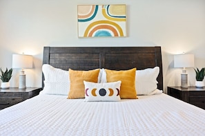 Een netjes opgemaakt bed met een witte deken, twee witte kussens en twee sierkussens met een rond patroon.