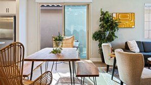 Un salon moderne avec une table à manger, des chaises et un canapé. Une porte-fenêtre coulissante donne accès à un balcon.