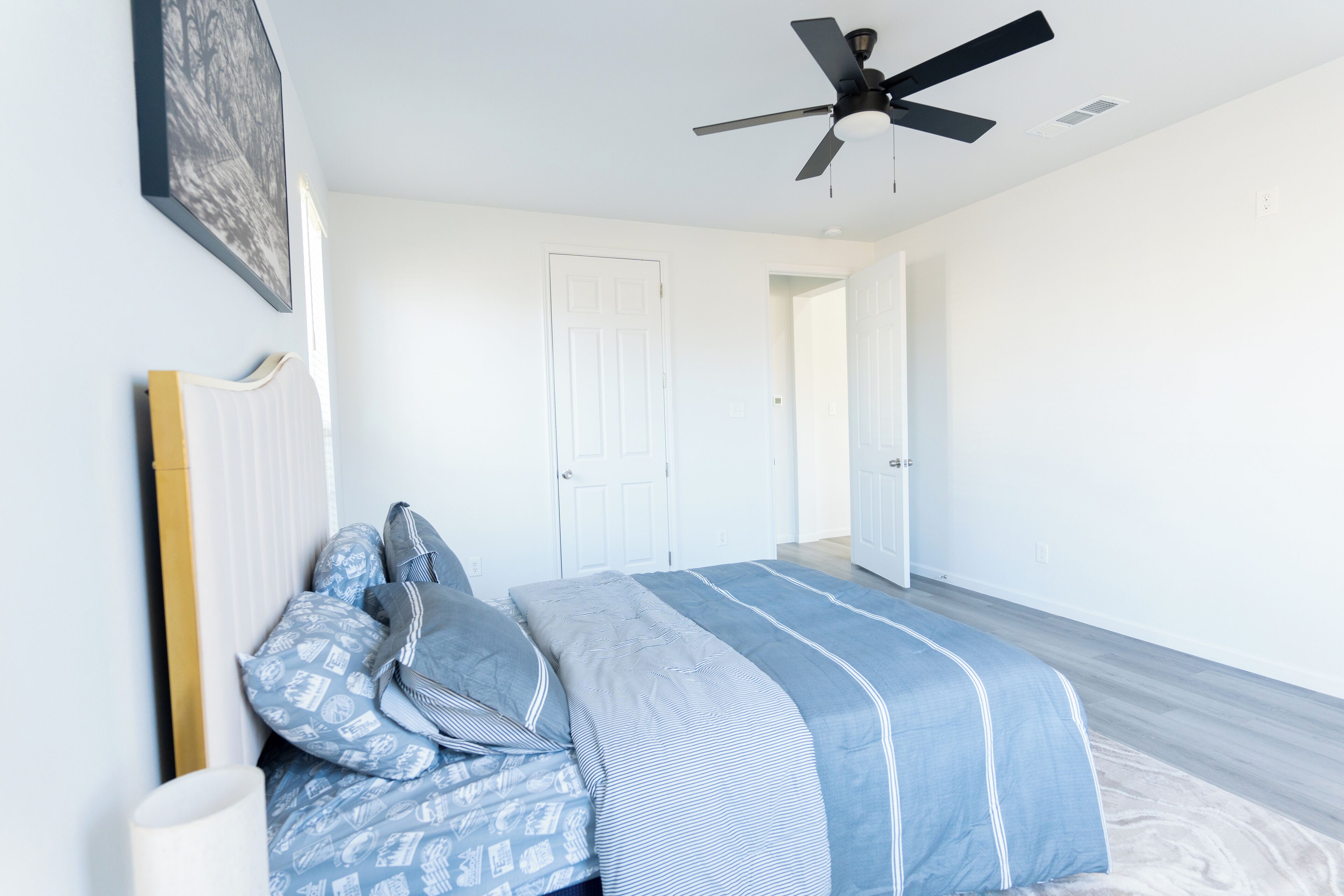 A bedroom with a bed, a ceiling fan, and a door leading to another room.
