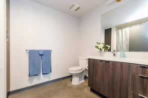 A bathroom with a toilet, a sink with a mirror, and a towel rack with two towels. - Lovely 3BR Apt w/ Balcony & Rooftop Pool + Views (Los Angeles)