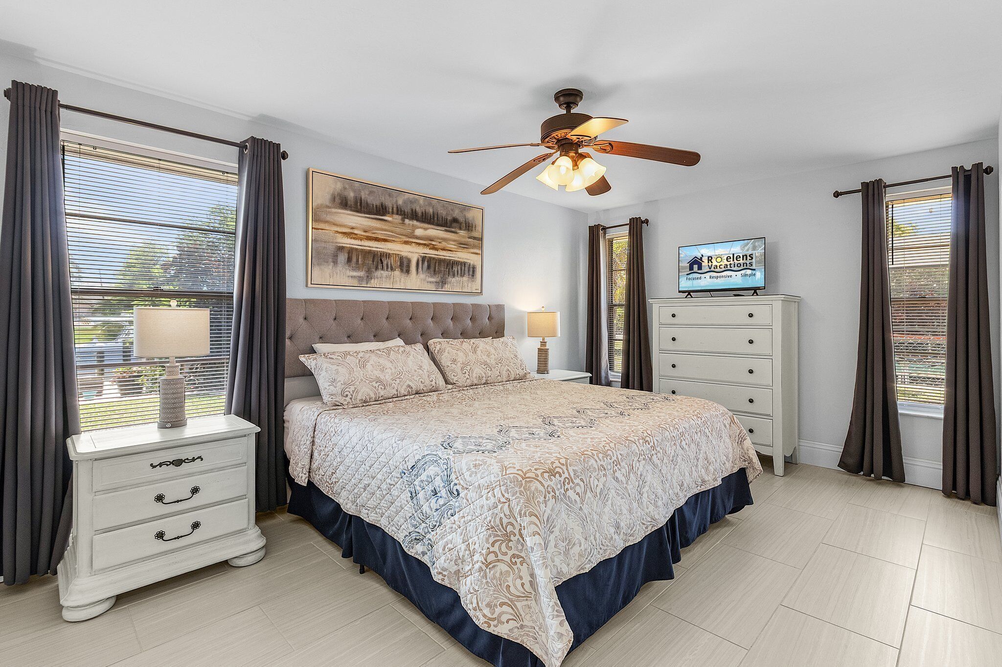 A bedroom with a bed, nightstands, a TV, and a ceiling fan.