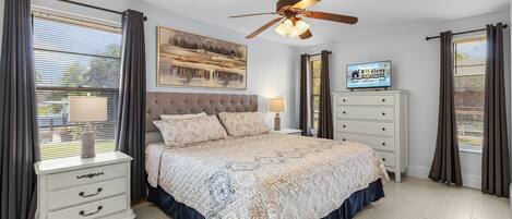 A bedroom with a bed, nightstands, a TV, and a ceiling fan.