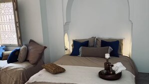 A bedroom with a bed, a window, and a decorative arch. - À l'ombre des orangers - "Touareg". (Marrakesh)