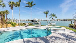 A swimming pool with lounge chairs and palm trees, surrounded by a waterfront view. - Welcome to Bluefin – Your Waterfront Getaway! (Treasure Island)