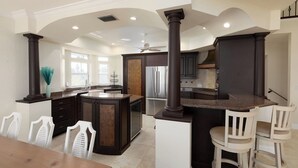 A spacious kitchen with dark cabinetry, a central island, and a dining area with white chairs. - Welcome to Bluefin – Your Waterfront Getaway! (Treasure Island)