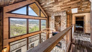 Amplia habitación con grandes ventanas que ofrecen vistas al exterior, techo de madera y chimenea de piedra.