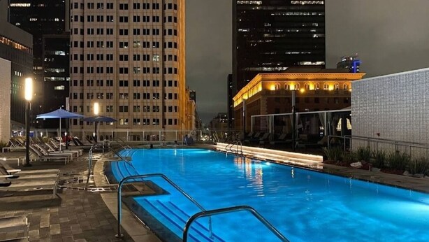 A nighttime swimming pool with lounge chairs and umbrellas, surrounded by high-rise buildings. - City Skyline Views 3-Bed High-rise Apartment w/Pool, Spa & Rooftop Views (Los Angeles)