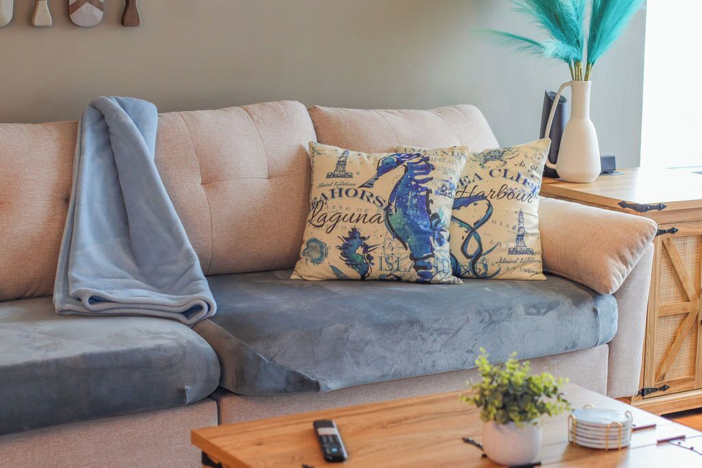 A living room with a sofa, a blanket, decorative pillows, a remote control, a small plant, and a wooden side table.