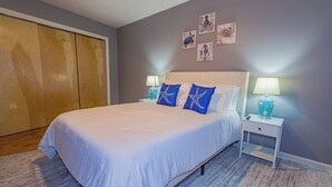 Une chambre à coucher avec un grand lit, deux tables de chevet avec des lampes, une armoire en bois et des œuvres d’art murales.