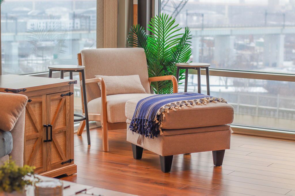 A modern living room with a large window, a sofa, an ottoman, and a wooden cabinet.