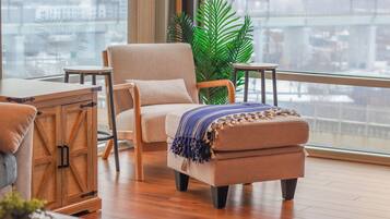 A modern living room with a large window, a sofa, an ottoman, and a wooden cabinet.