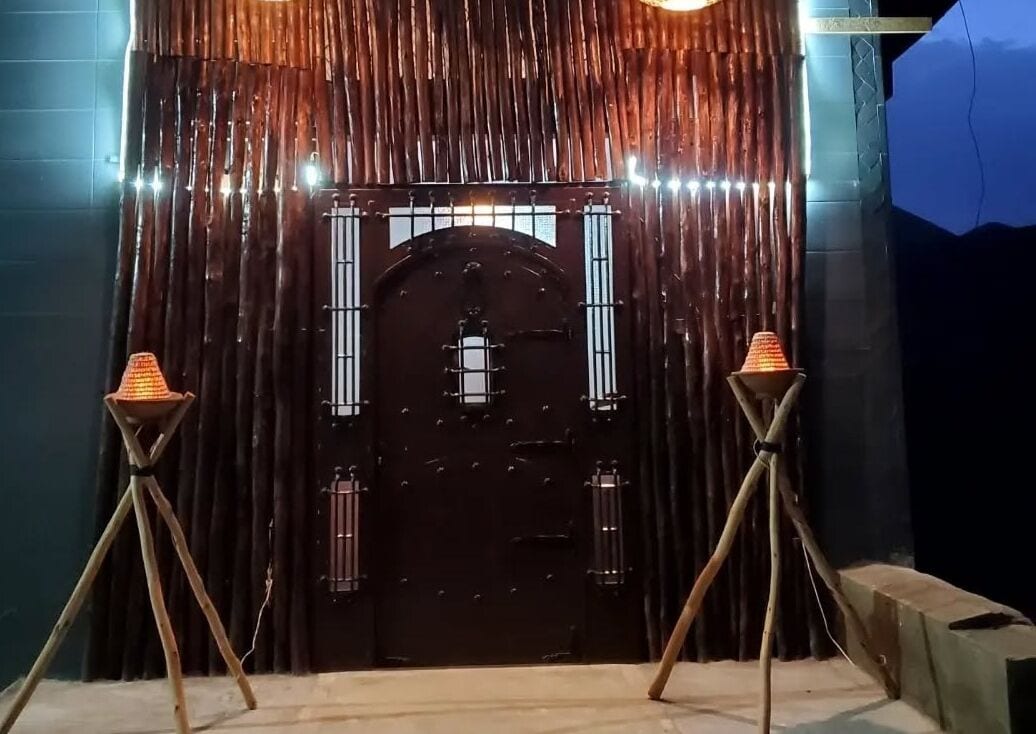 A dark wooden door with a metal gate, flanked by two standing lamps.