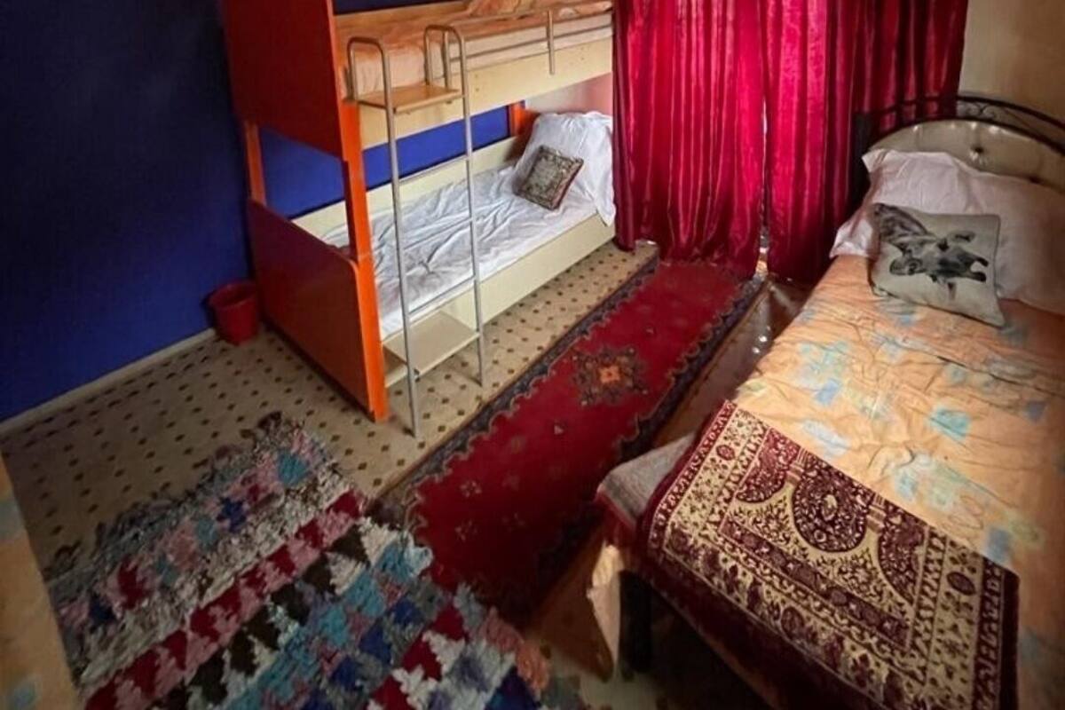 Une chambre avec un lit superposé, un lit simple, un tapis à motifs et un plafond en bois.