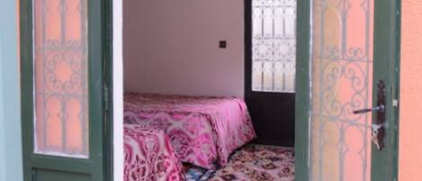 Una puerta abierta que da a un dormitorio con una colcha estampada y una ventana con barrotes decorativos.