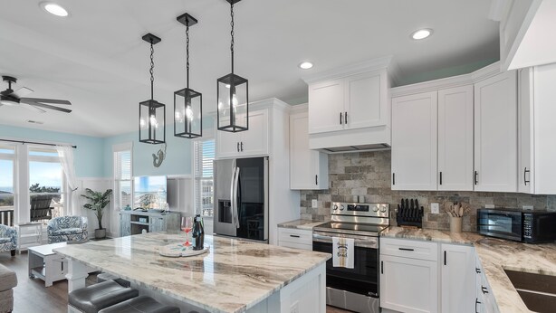 Una cocina moderna con armarios blancos, una isla de mármol, electrodomésticos de acero inoxidable e iluminación colgante.