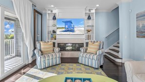 A living room with a fireplace, striped armchairs, and a view of a beach through a large window. - Beachside Haven | Steps from Siesta Beach – Stunning 3-Bedroom Townhouse with Pool (Siesta Key)