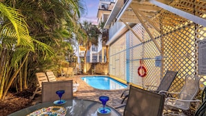 A pool area with lounge chairs, a glass table, and a poolside view of buildings and palm trees. - Beachside Haven | Steps from Siesta Beach – Stunning 3-Bedroom Townhouse with Pool (Siesta Key)