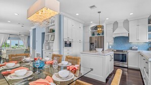A modern kitchen with white cabinets, a central island, and a dining area with wicker chairs and a glass table. - Beachside Haven | Steps from Siesta Beach – Stunning 3-Bedroom Townhouse with Pool (Siesta Key)