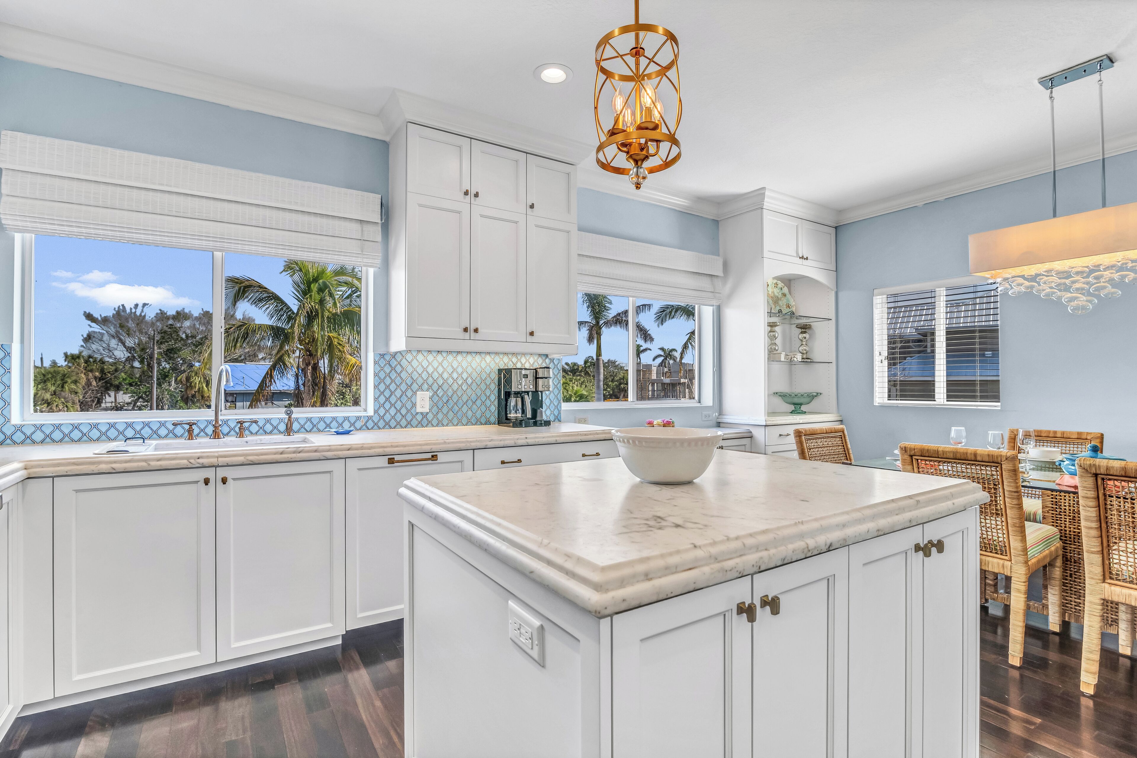 A kitchen with white cabinets, a marble island, and a dining area with wicker chairs.