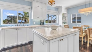 A kitchen with white cabinets, a marble island, and a dining area with wicker chairs. - Beachside Haven | Steps from Siesta Beach – Stunning 3-Bedroom Townhouse with Pool (Siesta Key)