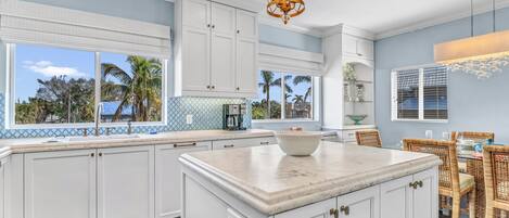 A kitchen with white cabinets, a marble island, and a dining area with wicker chairs.