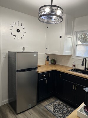 Una cocina moderna con refrigerador de acero inoxidable, encimera de madera, gabinetes negros, un lavaplatos integrado y un reloj decorativo en la pared.
