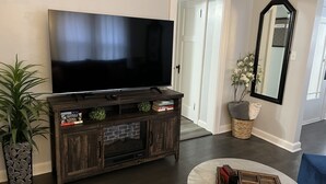 A living room with a large flat-screen TV on a wooden entertainment center, a potted plant, a mirror, and a round coffee table. - Black sheep cottage!
Charming 1 bedroom cottage in peaceful West Allis (West Allis)