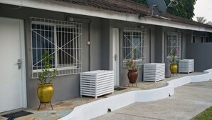 A building with a curved driveway, white doorways, and barred windows. There are potted plants and white crates outside. - Cool Villa Guest House (Sekondi-Takoradi)