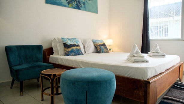 A bedroom with a bed, a chair, a small table, and a painting on the wall. - Cool Villa Guest House (Sekondi-Takoradi)
