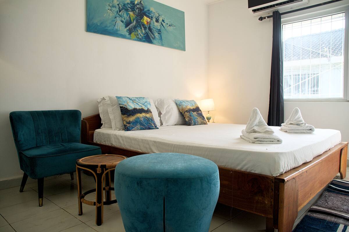 Un dormitorio con cama, una silla, una mesita y un cuadro en la pared.