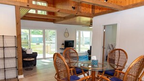 A dining area with a round glass table surrounded by wicker chairs with blue cushions, a television on a stand, and a view of the outdoors through large windows. - LakePointe Shores #4 -Beautiful cottage Madison on the Lake (Madison)