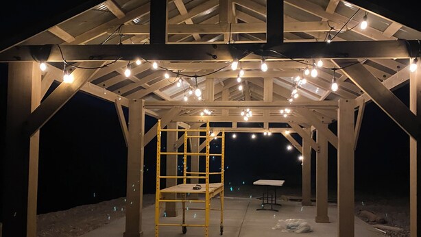 A covered outdoor area with a metal frame structure, a yellow ladder, and string lights.