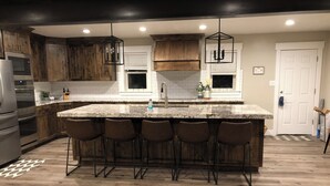 A modern kitchen with a large island, bar stools, wooden cabinets, and stainless steel appliances.